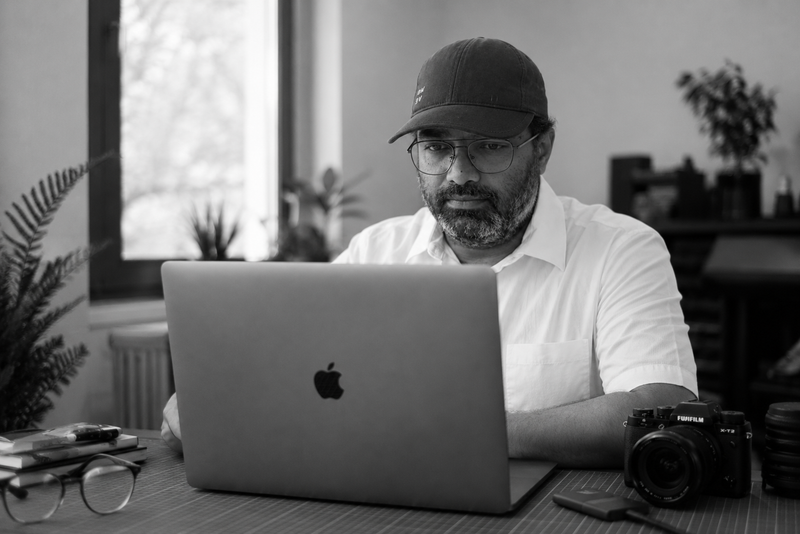 Ramesh using a laptop with an Apple logo in a casual setting at Codified Commerce.